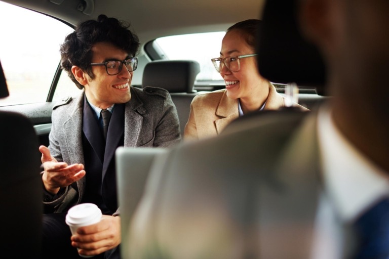 Man and woman professionally dressed speaking enthusiastically in the backseat of a car